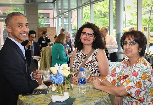 Alumni stand around a table, socializing at an event.